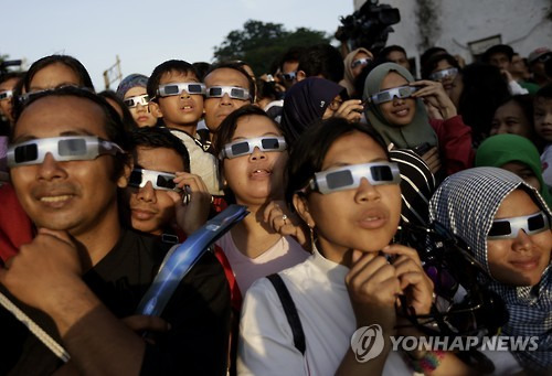 People look up at the sun wearing protective glasses to watch a solar eclipse in Jakarta, Indonesia, Wednesday, March 9, 2016. The rare astronomical event is being witnessed Wednesday along a narrow path that stretches across 12 provinces encompassing three times zones and about 40 million people. (AP Photo/Dita Alangkara)