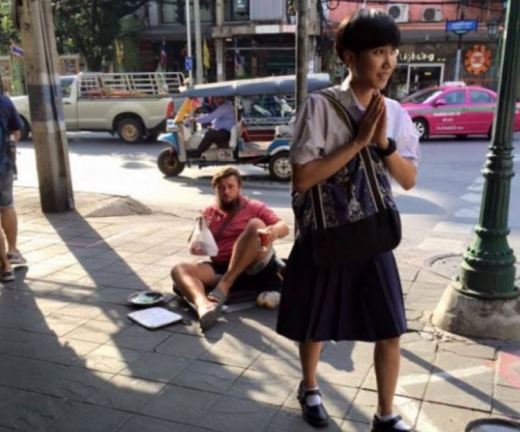 한 손에는 패스트푸드 음식을 든 서양 여행객이 방콕의 어느 거리에 앉아 여행자금을 구걸하고 있다. (사진=데일리메일 캡쳐)