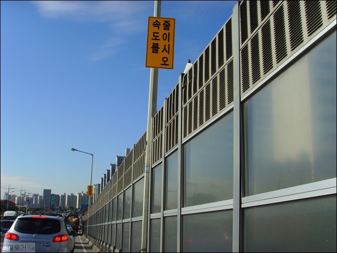 [사진] 차가 밀려서 찍을 수 있었던 도로 옆 방음벽 위의 “속도를 줄이시오.” 교통 안내 표지판