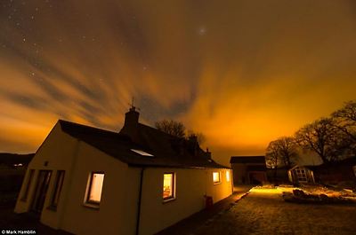 Mesmerising: A beautiful display of lights is pictured above the house in Carrbridge - giving the property warm yellow glow