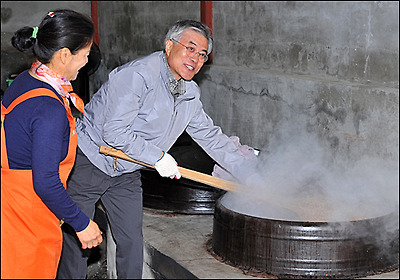  문재인 후보가 된장 콩이 익어가는 가마솥 안을 큰 주걱을 이용해 젖고 있다.