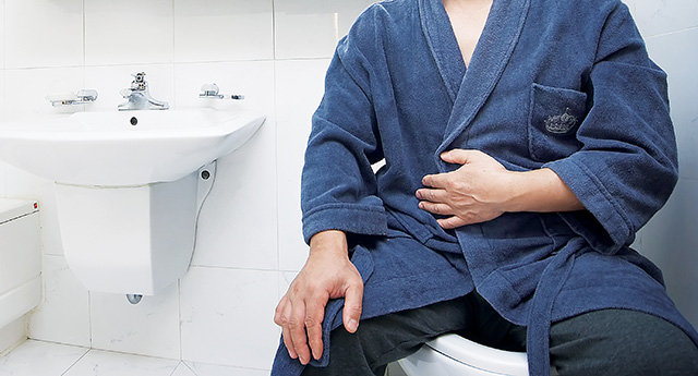 목욕 가운을 입은 남성이 변기에 앉아 있다.