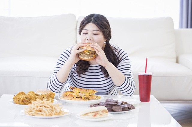여성이 햄버거를 먹고 있고, 식탁에는 음식이 많이 놓여 있다