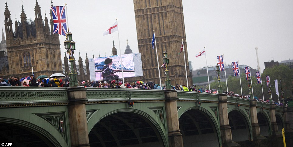 People take cover under their umbrellas on Westminster Bridge as images of the Queen are projected onto a screen
