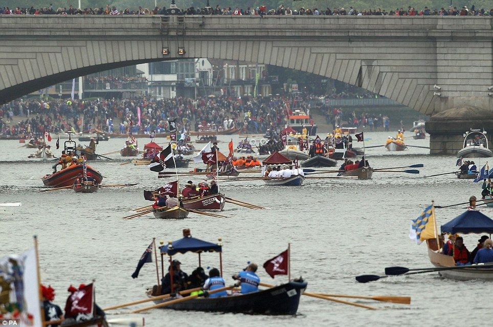 Crowds watch from the banks and the bridge as the boats prepare for the Queen's arrival