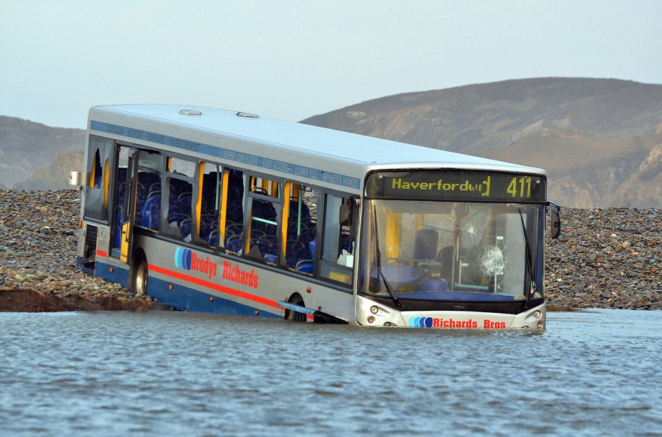 The bus which is partially lodged in a flooded field with its back wheels resting on the road in Newgale, Pembrokeshire, Wales