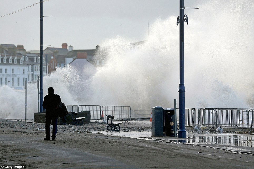 Walking along: Waves crash up against the sea defences at Aberystwyth during high tide and high winds