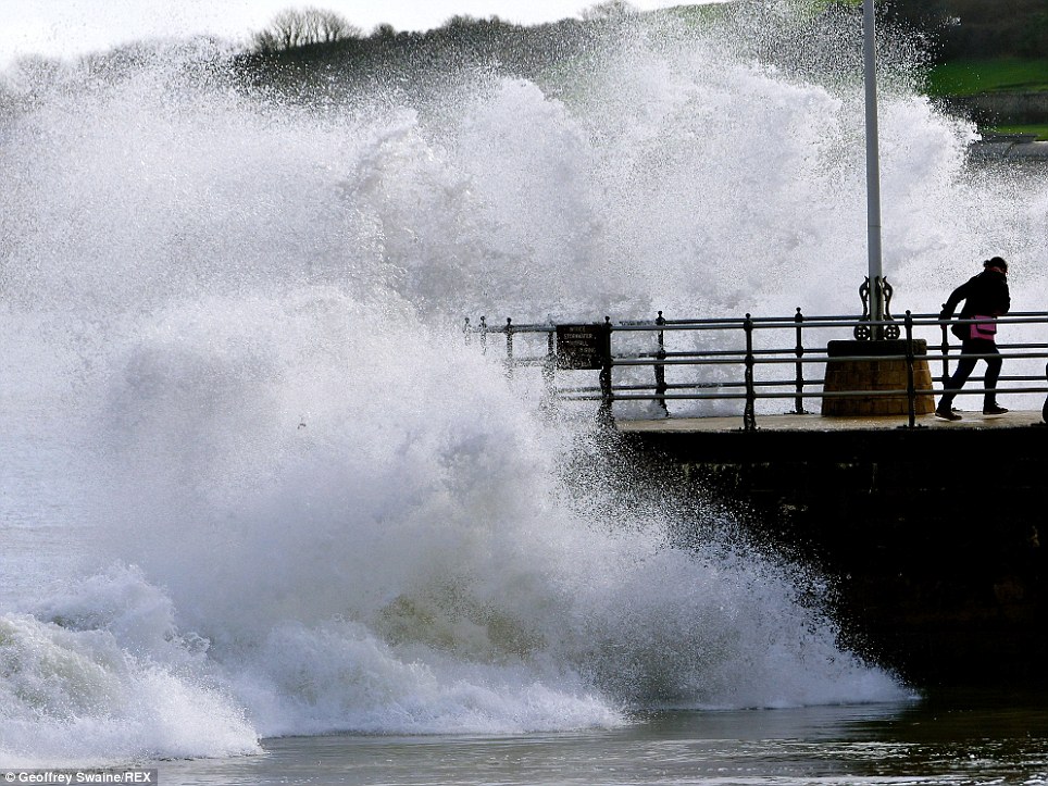 Running away: A woman flees large waves crashing against Swanage promenade in Dorset