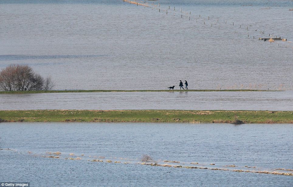 People walk with a dog on the banks of the flooded River Arun today near Amberley