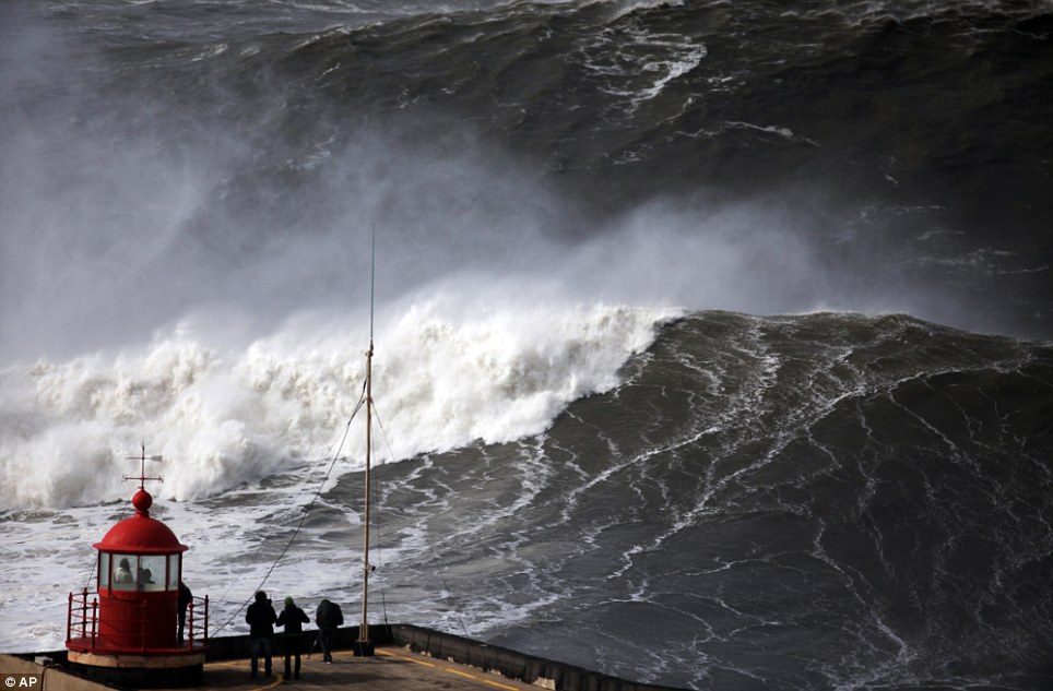 People watch huge waves approaching towards Nazare lighthouse, outside the fishing village of Nazare, in the central coast of Portugal