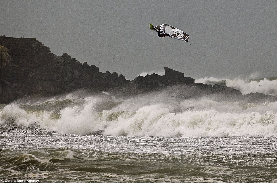 Up in the air: The weather is set to cause more misery for Britons - but it's not stopping these surfers making the most of the tidal surge in Cornwall