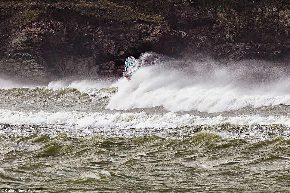 Extreme sport: Surfer Chris Murray hits the waves in Daymar Bay as windsurfers enjoy the giant waves caused by strong winds in Cornwall