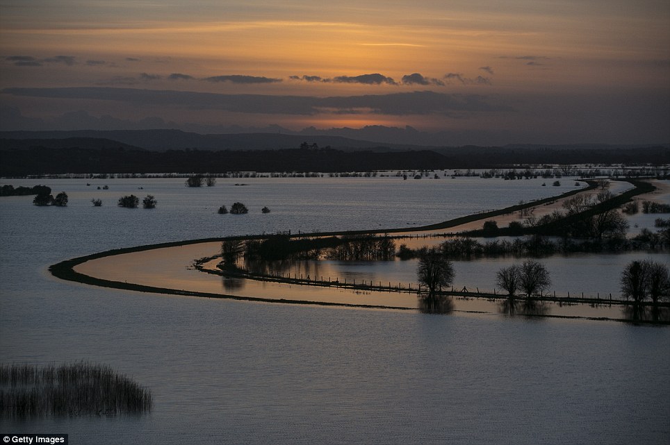 As it goes down: The sun sets over flooded fields surrounding the River Tone that has burst its banks in Somerset, viewed from Windmill Hill, in Stoke-St-Gregory