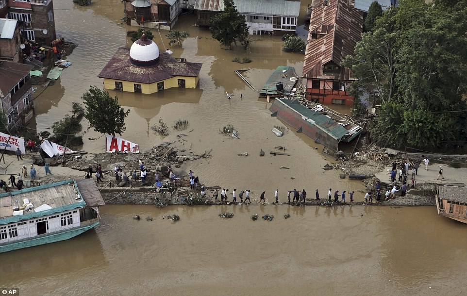Help: Kashmiri Muslims treading carefully today across the remains of a wall on the banks of the River Jehlum in Srinagar. More than 450 people have died in total