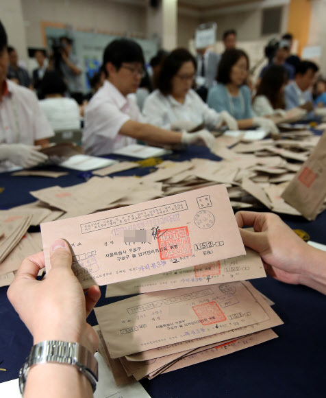 지난 21일 서울 종로구 선거연수원에서 진행된 ‘구로구청 투표함’ 계표 작업에 앞서 한 계표 사무원이 우편 투표함에서 나온 봉투를 확인하고 있다. 우체국 소인과 등기번호, 투표자가 쓴 자필 이름이 있어 진위 여부를 확인할 수 있다. 연합뉴스