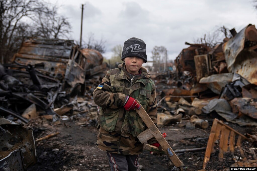 Yehor, 7, stands holding a wooden toy rifle next to destroyed Russian military vehicles near Chernihiv, Ukraine.