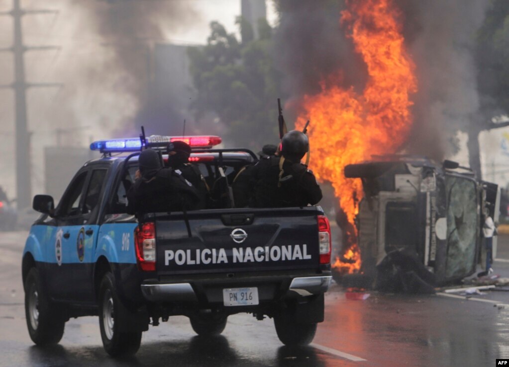 니카라과 마나과에서 반정부 시위가 벌어진 가운데, 무장한 경찰들이 불탄 경찰차 주변을 지나고 있다.