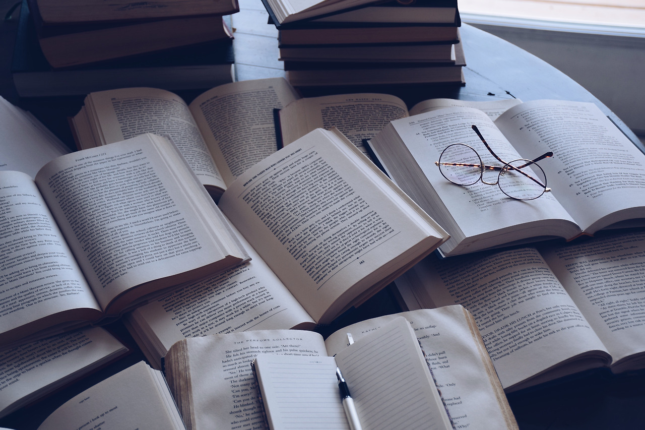 stacks-of-books-and-multiple-open-books-on-a-table-with-an-open-notebook-and-a-pen-and-reading_t20_9ljV4v.jpg