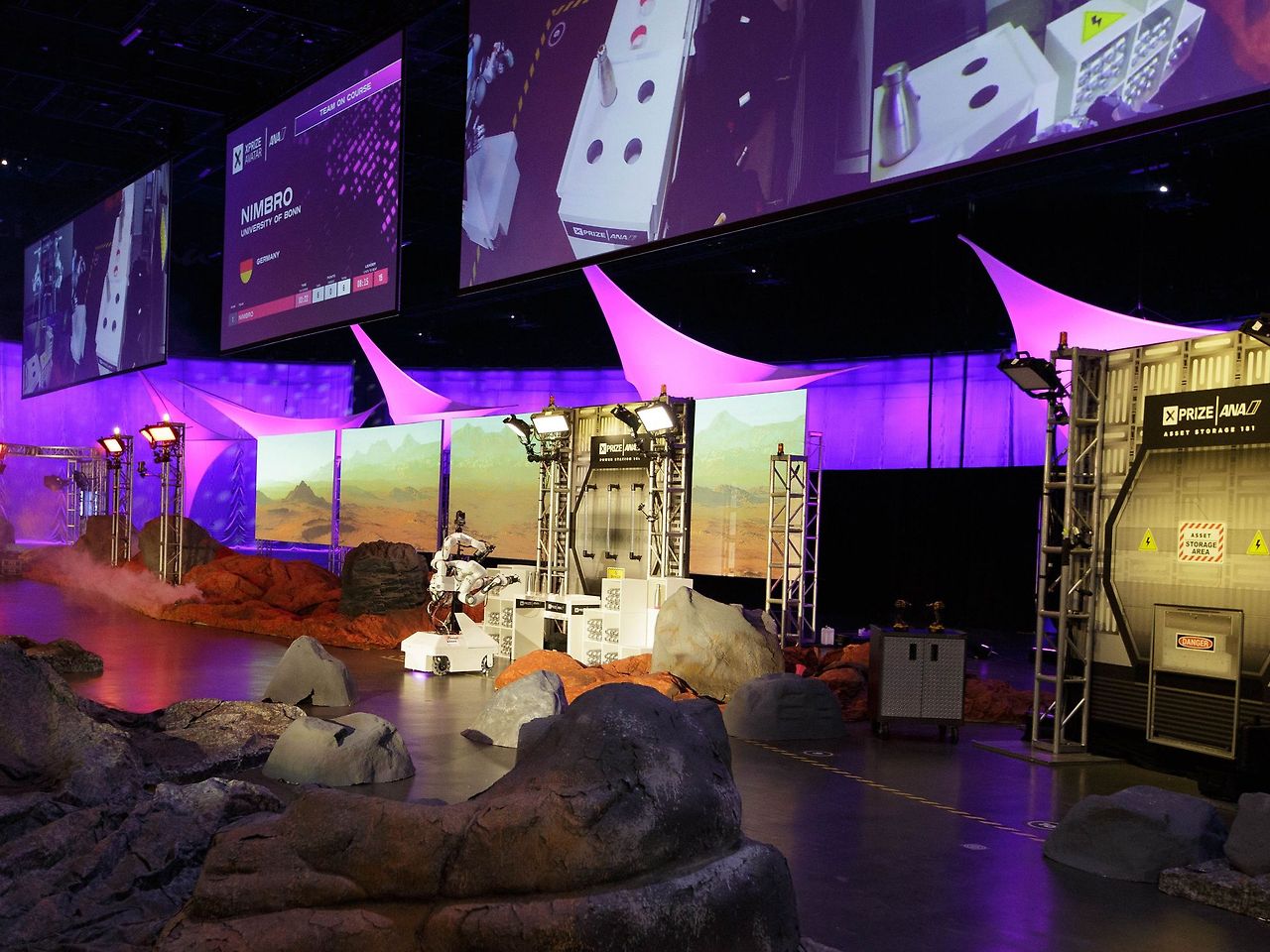 a-dramatically-lit-arena-with-decorative-alien-rocks-and-with-several-different-task-stations-for-the-robots-to-move-to.jpg