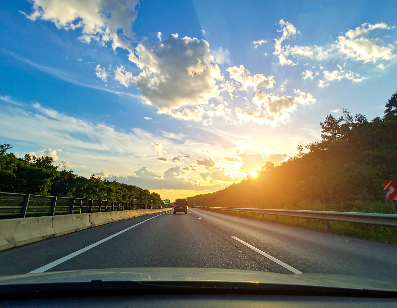 Firefly A beautiful view of warm sunlight and blue sky can be seen beyond a car driving on the highw.jpg