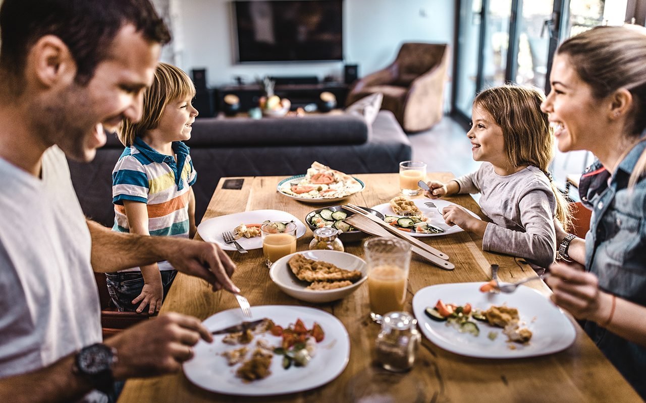 young-happy-family-talking-while-having-lunch-GettyImages-1132278686.jpg