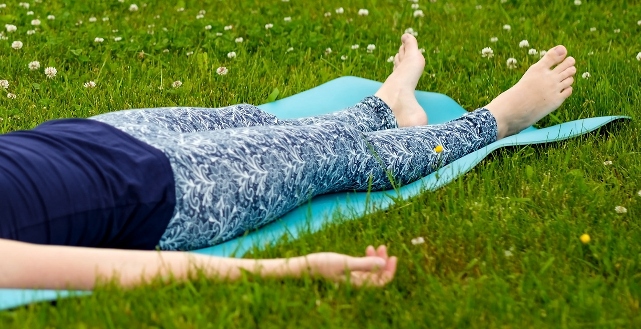 girl-doing-yoga-meditating-shavasana-corpse-position-park-green-grass.jpg