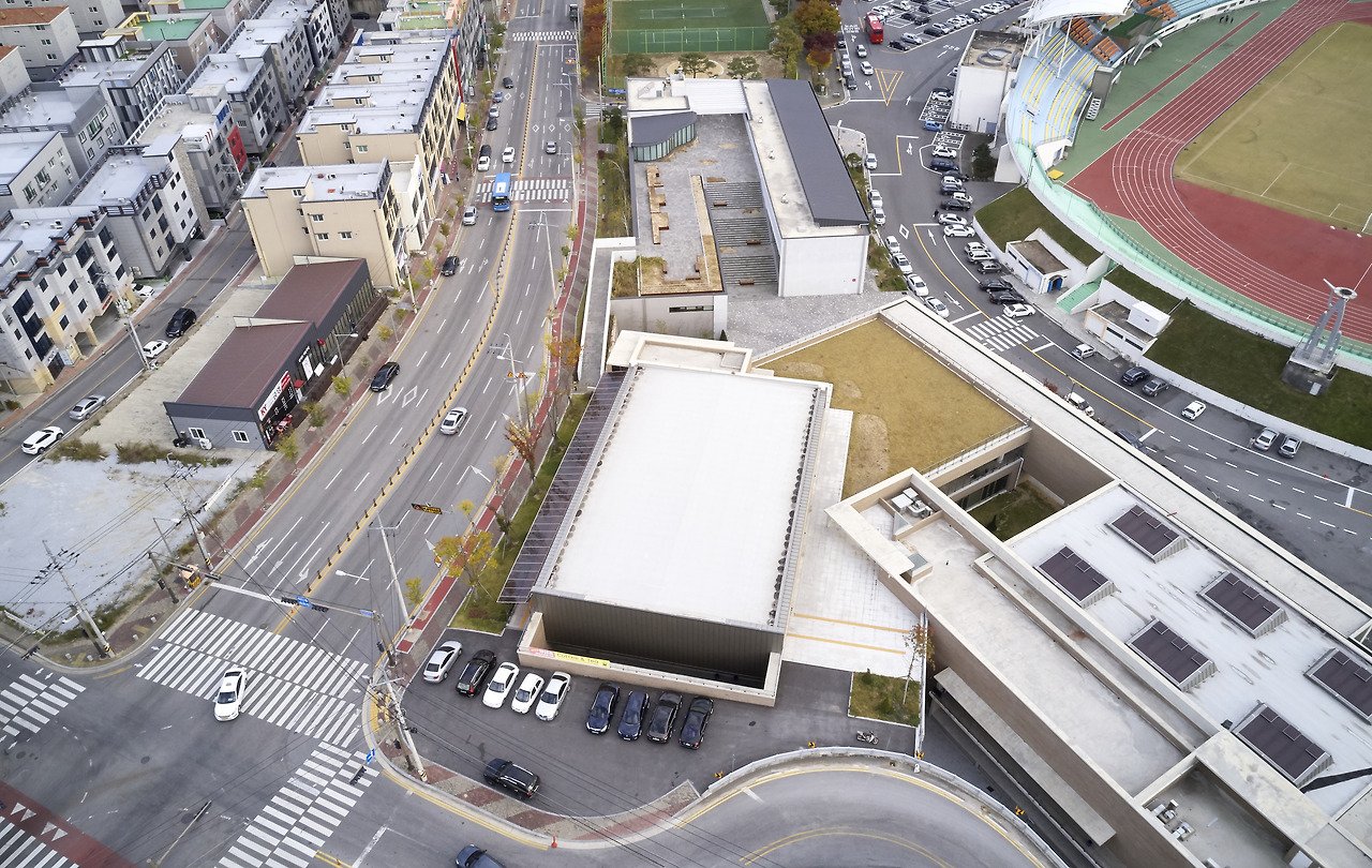 사진11_왼쪽 주택가와 차로를 사이에 두고 스포츠 콤플렉스가 있다. 황토책 천정가 채광창이 보이는 건축이 수영장이고 그 위로 천정에 짙은 회색구조물이 보이는 건축이 복싱훈련장이다..jpg