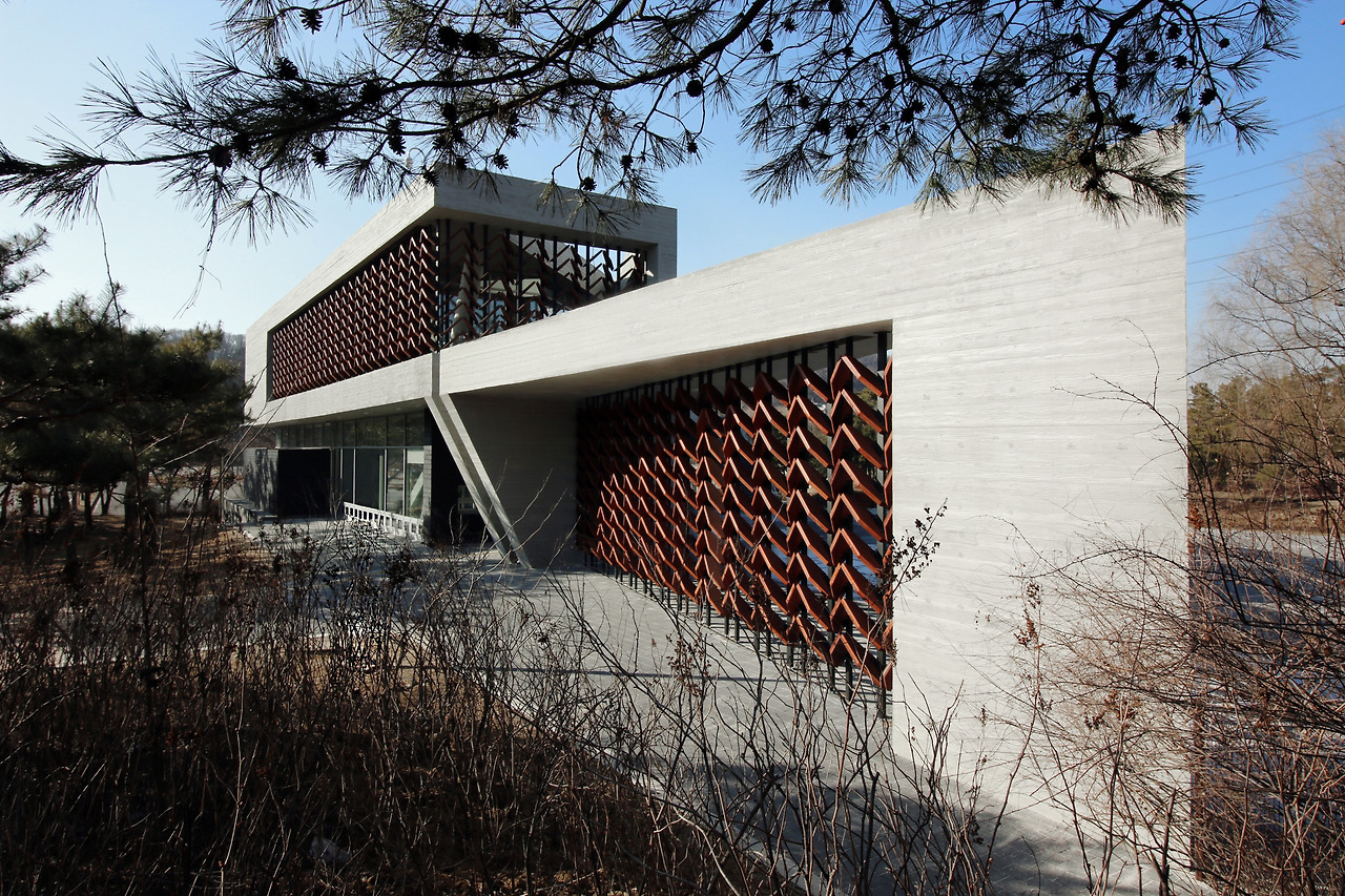 사진3_수목원의 출입구와 목연리 본관 2층에 길게 도열한 열주 형태의 목재 스크린. 가까이서 보면 붉은빛 도는 ∧형태의 목재가 8단 또는 9단으로 겹겹이 포개져 있다.  Softarchitecturelab 제공.jpg