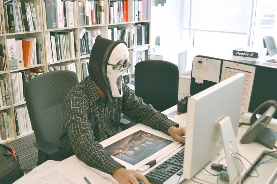 a-man-wearing-a-mask-and-glasses-sitting-at-a-desk.jpg