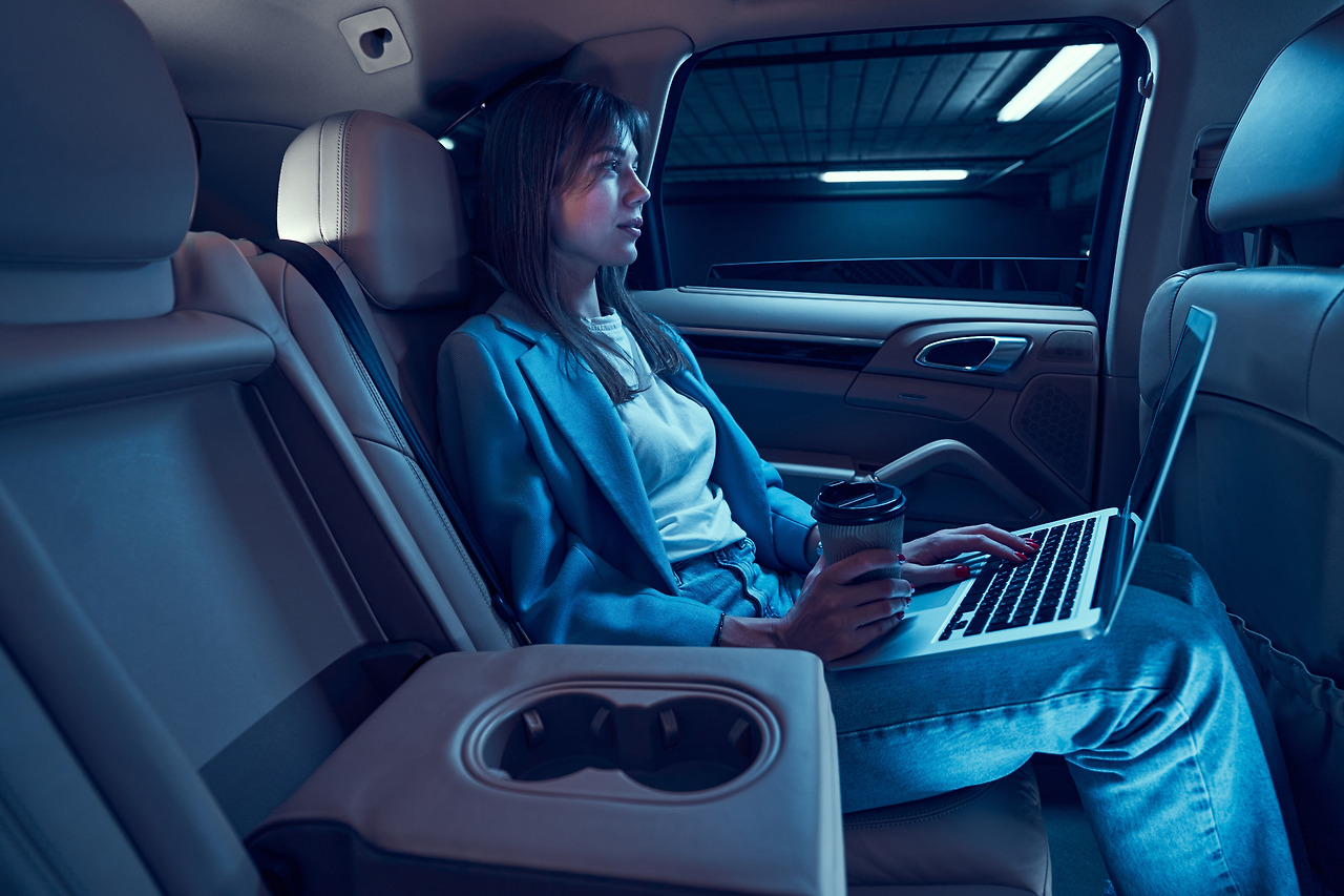 woman-drinking-coffee-and-using-laptop-in-car-2023-11-27-05-06-25-utc.jpg