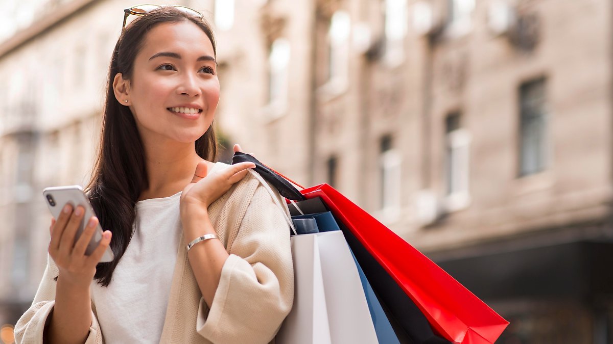 smiley-woman-holding-shopping-bags-smartphone-outdoors.jpg