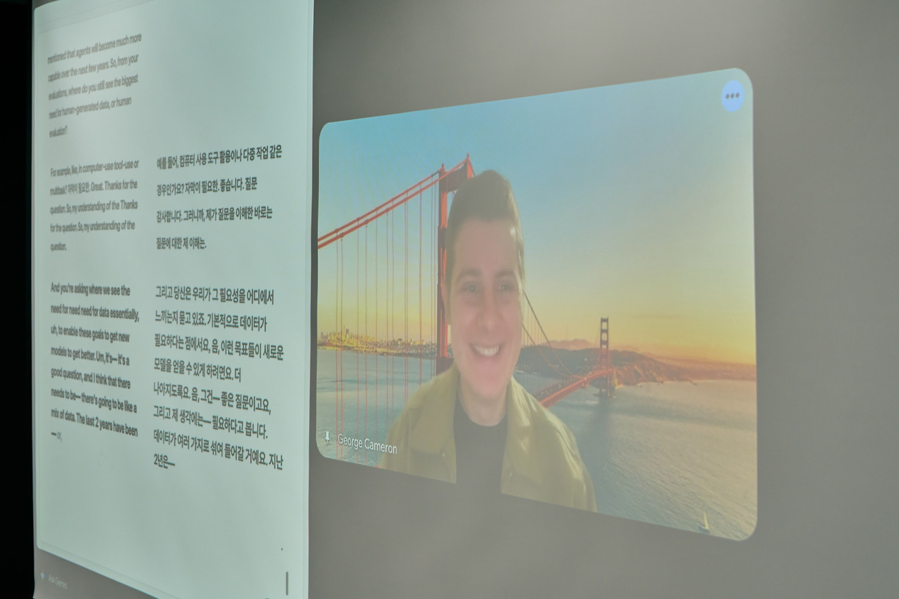 The projected video call for the remote keynote, the speaker on a Golden Gate Bridge background beside a live transcript.