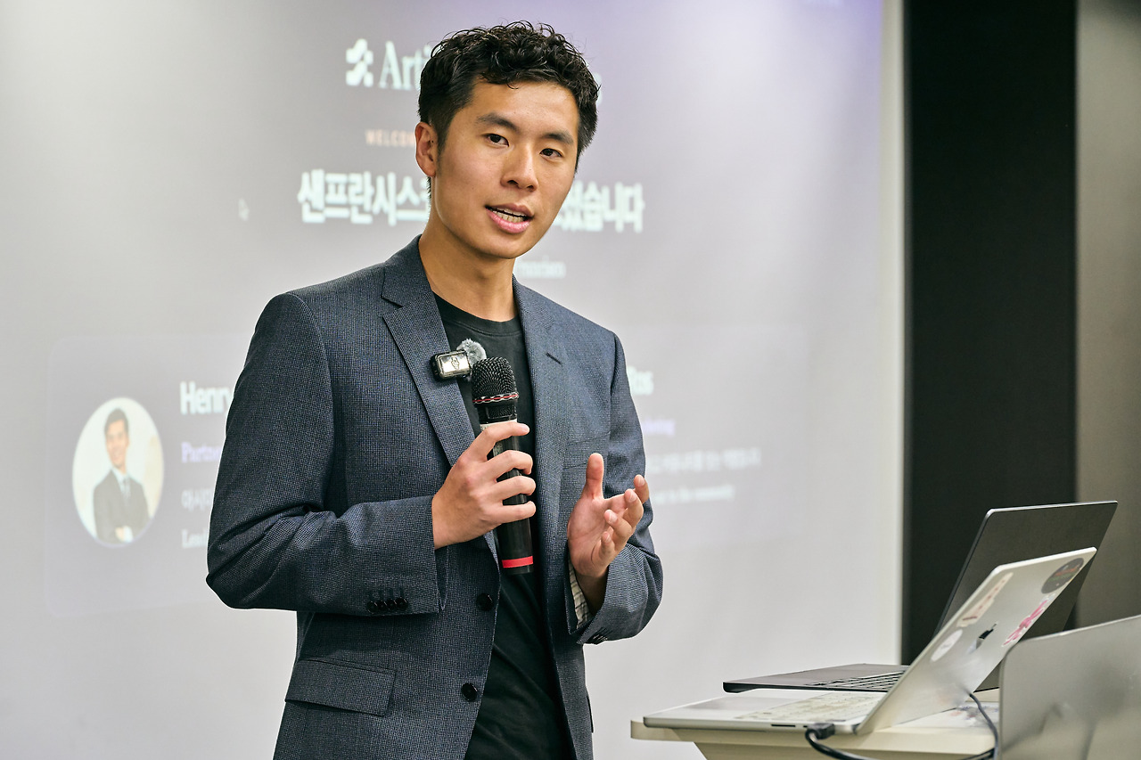 A speaker opening the event with a microphone, the Artificial Analysis wordmark projected behind him.