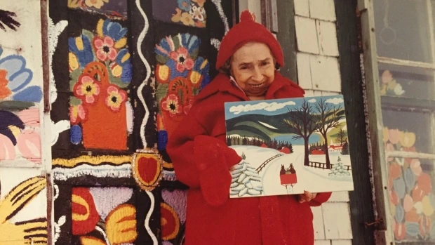 maud-lewis-posts-with-one-of-her-paintings-standing-in-front-of-her-art-house.JPG