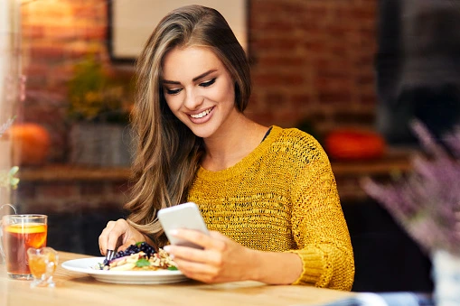 beautiful-smiling-young-woman-looking-at-phone-while-sitting-and-eating-in-a-cafe.jpg?b=1&s=170667a&w=0&k=20&c=EQvOt9CUAYvrmn9nxN_xunInK3avSCSFfxoPtm16G5s=
