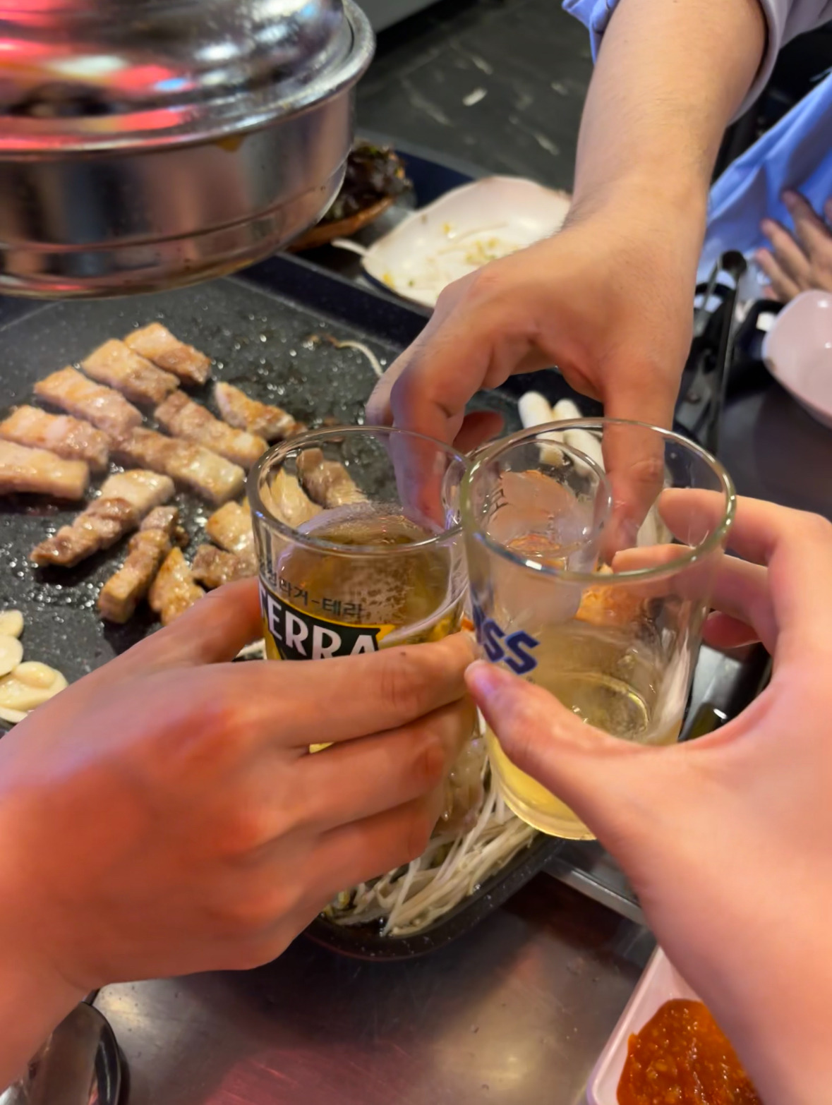 불판 앞에서 맥주잔을 맞대며 건배하는 장면