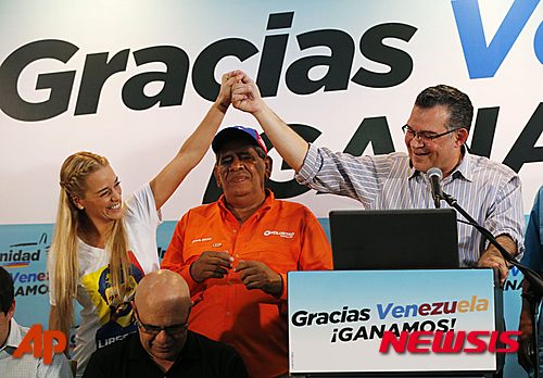 Lilian Tintori, wife of jailed opposition leader Leopoldo Lopez, left, holds hands up with reelected opposition lawmaker Enrique Marquez, who represents Zulia state, during a press conference in Caracas, Venezuela, Monday, Dec. 7, 2015. Venezuela's opposition won control of the National Assembly by a landslide in Sunday's election, stunning the ruling party and altering the balance of power 17 years after the late Hugo Chavez was elected president. (AP Photo/Ariana Cubillos)