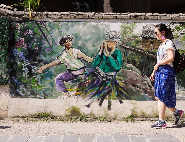 먀오족의 생활상을 그린 벽 앞을 지나가는 여행자.