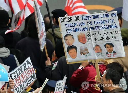 일본 도쿄 도심에서 벌어진 시위 참가자가 든 팻말에 '사기, 위선, 명예훼손, 선전으로 사는 이들을 저주한다'(Curse on those who live on deception and hypocrisy, defamation and propaganda.)는 글과 고노 요헤이(河野洋平) 전 일본 중의원 의장, 박근혜 대통령, 일본군 위안부 소녀상, 우에무라 다카시(植村隆) 전 아사히(朝日)신문 기자 등의 얼굴이 담겨 있다. 또 매국노, 사기꾼, 걸식, 매춘부 등의 단어가 함께 적혀 있다. [연합뉴스 자료사진]