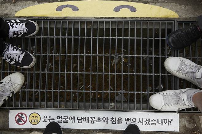 `씩~ 웃는 스마일` 스티커가 붙어있는 빗물받이 하수구 주변으로 사람들이 모여있다. [제임스 요한슨 객원 사진작가]
