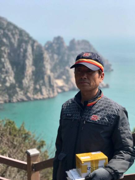 홍도에서 태어난 정씨가 우편물을 배달하다 잠시 홍도의 멋진 바다를 배경으로 포즈를 취하고 있다.