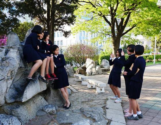 평양 대동문 인근에서 핸드폰 사진을 찍고 있는 북한 여고생들. 턱을 괴고 팔을 마주잡으며 포즈를 취한 친구를 보며 한 여학생이 박장대소하고 있다.[Sejin Pak 페이스북]