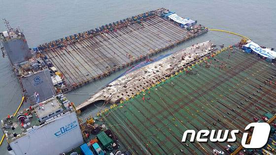 23일 오전 전남 진도군 동거차도 앞바다에서 세월호 인양 작업 중인 재킹바지선 사이로 선체 우측면이 모습을 드러내 상하이 샐비지 관계자들이 고박작업을 하고 있다. 세월호가 침몰 1073일만에 수면 위로 모습을 드러냈다. 해양수산부는 이날 새벽 3시 45분께 스태빌라이저로 추정되는 세월호 선체 일부가 수면에서 육안으로 보이기 시작한데 이어 약 1시간 후인 새벽 4시 47분께 본체가 드러났다고 밝혔다. (서해해경본부 제공) 2017.3.23/뉴스1