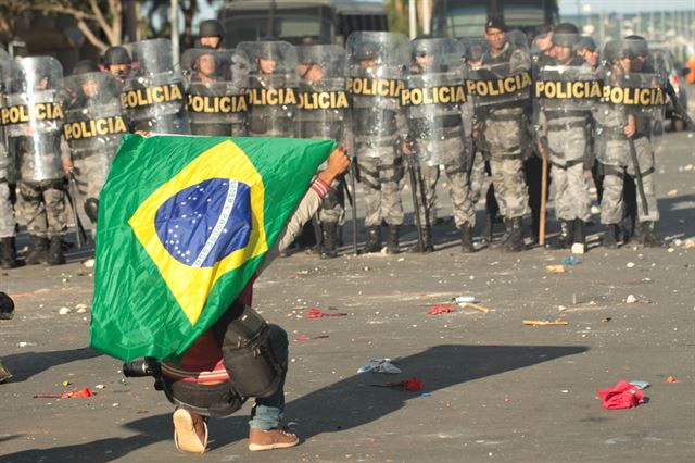 24일 브라질 수도 브라질리아에서 열린 미셰우 테메르 대통령의 퇴진을 요구하는 시위에 참석한 한 남성이 브라질 깃발을 들고 거리에 앉아 무장경찰을 바라보고 있다. 브라질리아=EPA 연합뉴스