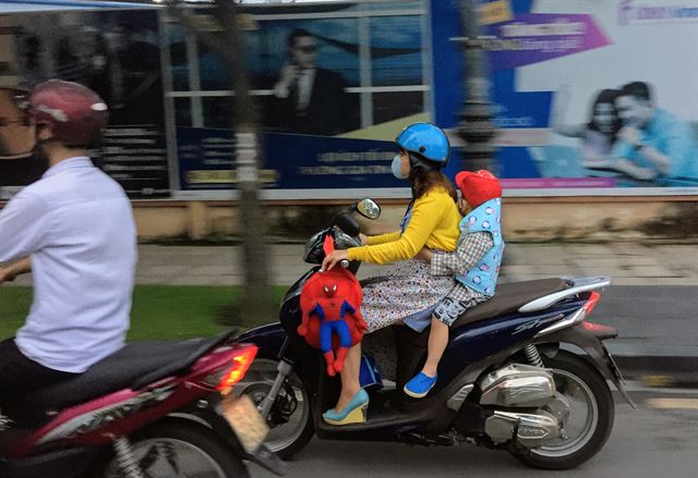 한 어머니가 오토바이 뒤에 앉은 아이가 떨어지지 않도록 아기띠를 두른 채 달리고 있다.