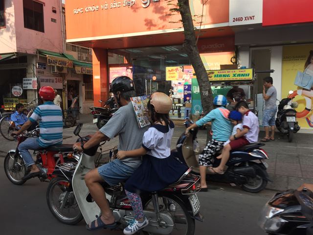 한 학생이 오토바이로 이동하는 동안 책을 읽고 있다. 베트남에서는 오토바이 위에서 다양한 일들이 이뤄진다.