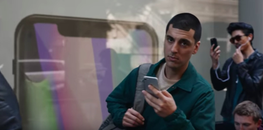광고 마지막 장면. 남자 주인공이 애플스토어앞에 아이폰X를 구입하려고 기다리는 사람과 눈이 마주친다. 이 사람의 헤어스타일이 M자 형태로 뒷배경의 아이폰X의 M자 형 디스플레이와 비교된다. /삼성전자 모바일 USA 캡처