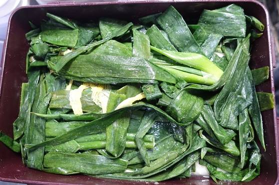 대파의 거친 잎으로 덮인 채 익어가는 백김치. 김치말이국수에 들어간다.