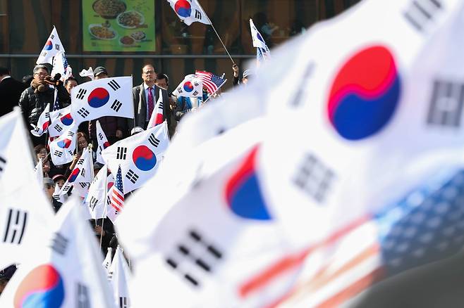 3일 오후 서울 용산구 서울역광장에서 열린 박근혜 전 대통령 탄핵 무효 석방 촉구 집회에서 시민들이 보수단체 회원들이 흔드는 태극기를 바라보고 있다. [뉴스1]