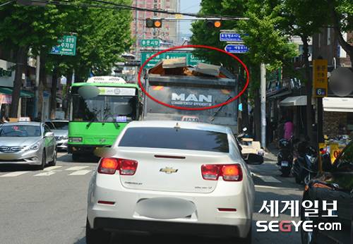 지난달 27일 서울 용산구 한 재래시장 이면도로. 25톤 덤프트럭이 덮개를 제대로 덮지 않은 상태에서 주행하고 있다. 뒤따르는 운전자의 안전을 위협 하고 있어 단속이 절실한 실정이다.